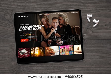 Sample TV series and movies streaming app on digital tablet and wireless earbuds on the table.