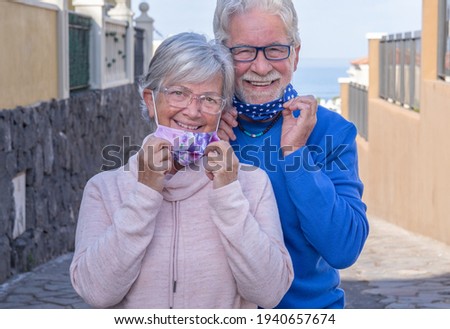 Attractive senior couple already vaccinated against coronavirus contagion - smiling outdoors taking off protective masks Royalty-Free Stock Photo #1940657674