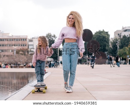 Mother and daughter playing on skateboard. very happy faces of woman and girl. same colour  of clothes, get fun outdoor in weekend. Small kid study skating. 