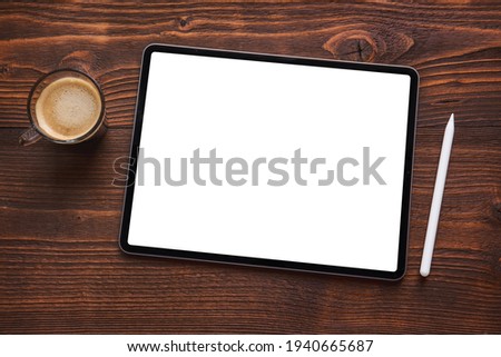 Cup of coffee next to tablet computer with blank white screen and wireless stylus pen for drawing and writing on the screen.
