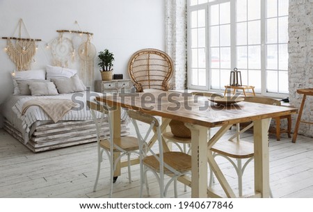 The interior of a large modern living room with a dining table, a bed and large windows flooded with light
