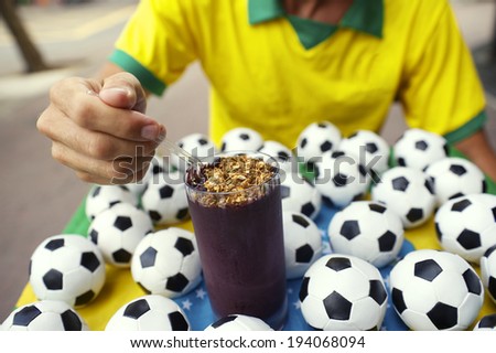 Brazilian football player sitting eating acai in a glass surrounded by soccer balls