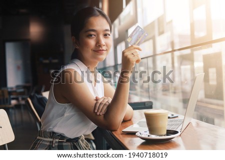 Beautiful  Asian woman holding credit card and using laptop while drinking coffee. Businesswoman working at cafe ,Online shopping, internet banking, spending money, work from home concept.