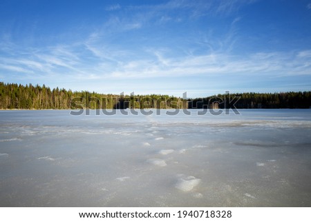 Surface of lake landscape with melting ice in early spring. Beautiful blue sky with clouds. Finland.
