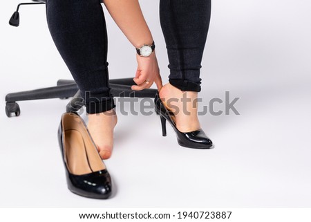 Cropped photo of female hands putting black, fashion , lacquer heeled shoes on her foot. Businesswoman wearing formal shoes in office, gray background