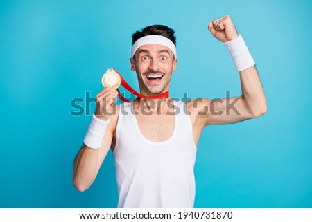 Photo of young excited sportsman happy smile win competition hold gold metal fists hand isolated over blue color background