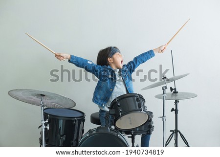 Little Asian boy plays the drums in studio with state of excitement against light gray background Royalty-Free Stock Photo #1940734819