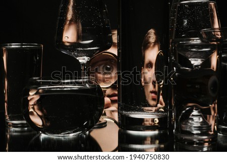man looking through a magnifying glass and glasses of water with reflections and distortions
