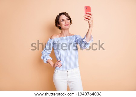 Photo portrait of smiling woman taking selfie holding phone in one hand isolated on pastel beige colored background