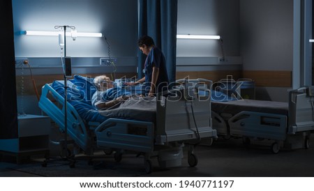 Hospital Ward: Portrait of Elderly Man Wearing Oxygen Mask Resting in Bed, Struggling to Recover after Covid-19, Sickness, Disease, Surgery. Old Man Fighting for His Life. Dark Blue Sad Shot Royalty-Free Stock Photo #1940771197
