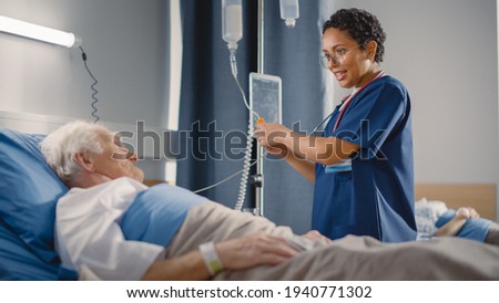 Hospital Ward: Friendly Female Head Nurse Making Rounds does Checkup on Elderly Patient Resting in Bed. She Checks Computer for Vitals while Old Man Fully Recovering after Successful Surgery