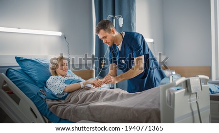 Hospital Ward: Friendly Head Nurse Connects Finger Heart Rate Monitor or Pulse Oximeter to Beautiful Female Patient Resting in Bed. Nurse Does Patient Checkup After Successful Surgery. Modern Clinic Royalty-Free Stock Photo #1940771365