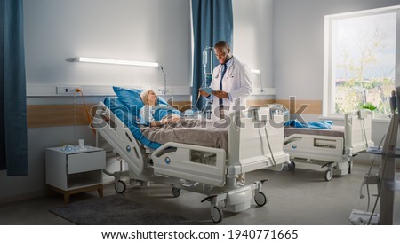 Hospital Ward: Friendly Black Doctor Talks to Beautiful Caucasian Female Patient Resting in Bed. Physician Uses Tablet Computer, Explains Test Results. Woman Recovering after Successful Surgery Royalty-Free Stock Photo #1940771665