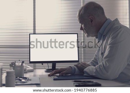Doctor sitting at desk in his office and staring at the computer screen, blank copy space