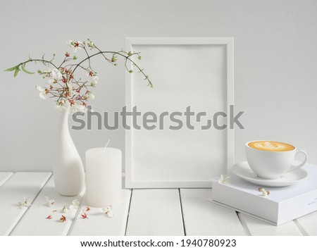 Blank mockup picture frame,coffee cup ,candle and beautiful Nodding Clerodendron flowers in modern ceramicvase on wood table  white wood background,breakfast in white room interior