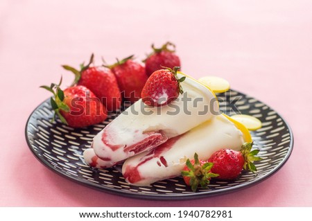 Creamy ice cream with fresh strawberries on a stick cooked at home lying on a black plate on a pink tablecloth, background