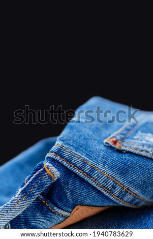 Folded blue jeans close-up with copy space for text on black vertically background, comfortable casual pants and clothing. Denim cotton fabric with pocket, leather label and orange thread seams.