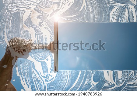 Window cleaner using a squeegee to wash a window with clear blue sky Royalty-Free Stock Photo #1940783926