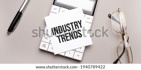 pen, calculator and glasses on grey background. Business concept. White paper sheet with INDUSTRY TRENDS sign