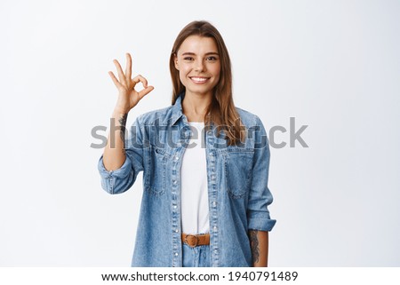 Very good. Smiling young blond woman showing okay sign and looking satisfied, approve good thing, standing satisfied against white background, praise product