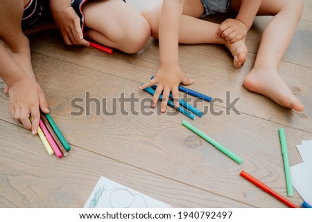 Siblings drawing with colored markers while lying on wooden floror at home in the living room. Arts and crafts for kids. Paint on children hands. Creative little artist at work.