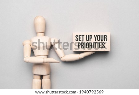 Wooden man shows with a hand to white board with text Set up your priorities,concept