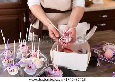 A woman packs pictures in a festive box. She's holding a dessert.
