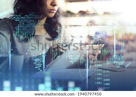 Office woman with tablet in hands, working in blurry office background with double exposure of world map and graph dynamics, candlesticks rising. Concept of stock market and finance