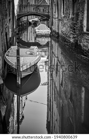 Small canal in Venice with bridge and moored boats, Italy. Black and white urban photography, venetian view
