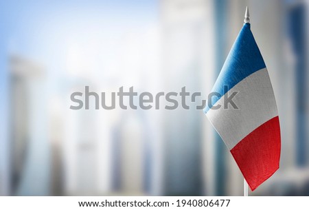 A small flag of France on the background of an urban abstract blurred background.