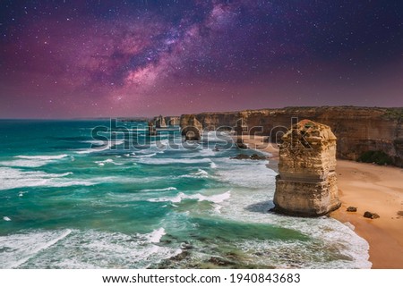 Blue green ocean and beach landscape with sandbanks cliffs and waves with close view of The twelve apostles and cliffs at night in Victoria, Australia against a sky with beautiful colors of Milky Way Royalty-Free Stock Photo #1940843683