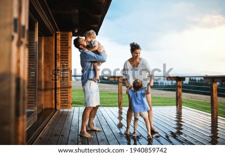 Family with small children playing in rain on patio by wooden cabin, holiday in nature concept. Royalty-Free Stock Photo #1940859742