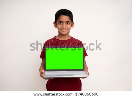 Young indian kid holding a laptop with green screen and standing on a white isolated background with copy space.