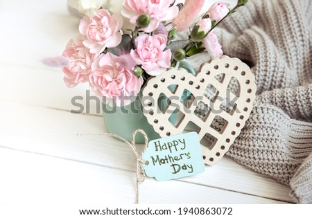 A festive composition with fresh flowers in a vase, decorative elements and a wish for a happy mother's day on a postcard.