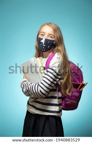 Schoolgirl girl in a protective mask with a backpack on a blue background. Studio shot. High quality photo
