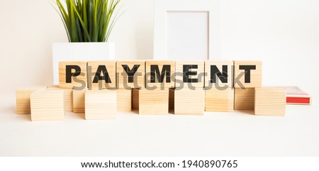 Wooden cubes with letters on a white table. The word is PAYMENT. White background with photo frame, house plant.