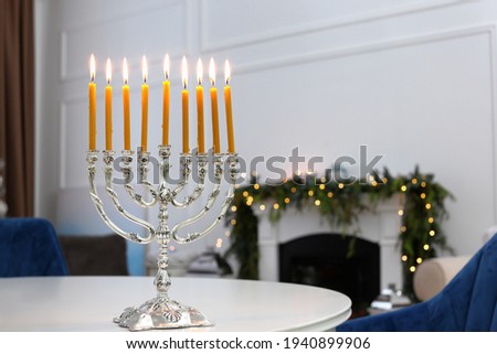 Silver menorah on white table in room with fireplace and Christmas decorations. Hanukkah symbol