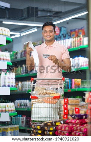 Happy young man holding credit card at grocery store.  Royalty-Free Stock Photo #1940921020