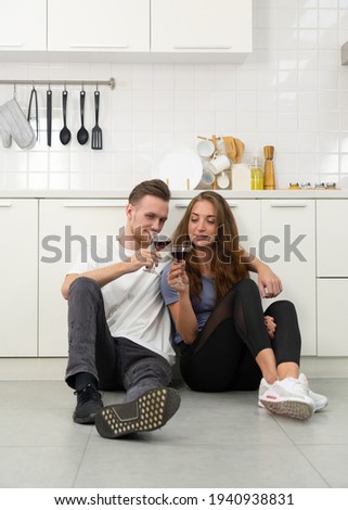 authentic picture of young caucasian couple sitting in the kitchen together and drinking wine for lunch in anniversary day