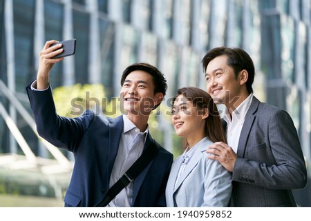 team of three asian businesspeople taking a selfie in downtown financial district of modern city