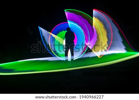 one person standing against beautiful green and blue circle light painting as the backdrop