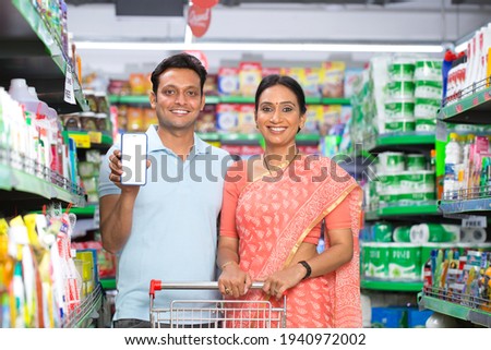Happy couple showing blank screen of mobile phone at grocery store  Royalty-Free Stock Photo #1940972002