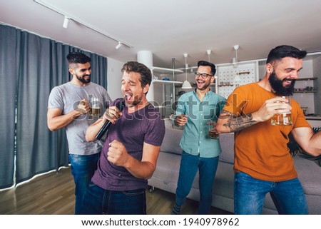 Group of young men spend free time in karaoke, sing and have fun together, with friends, at home.
