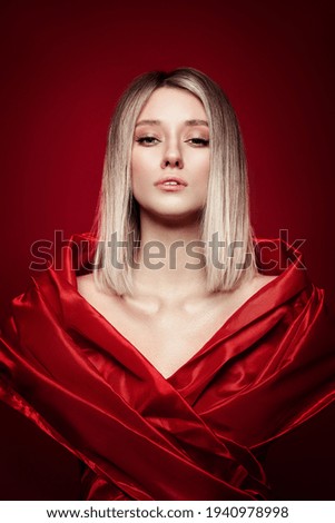 Woman with colored hair color of a blonde in red dress on red background. Coloring blond hair woman model in ash color. Portrait of a girl