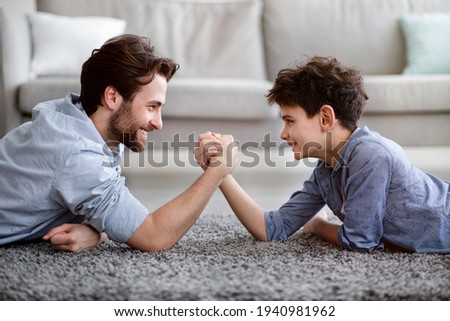 Happy father competing in arm-wrestling with his son, enjoying time together at home, side view