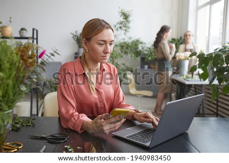 Portrait of successful young businesswoman using computer in flower shop while managing small business, copy space