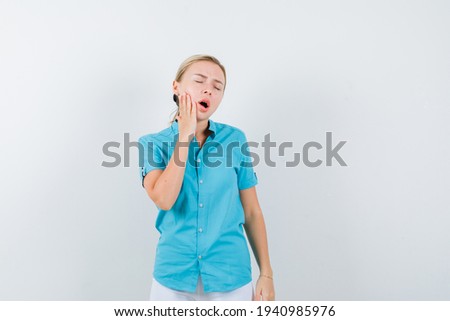  blonde woman suffering from toothache in blue blouse and looking painful , front view. 