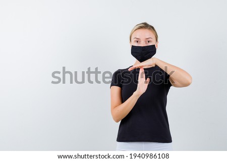  blonde lady showing time break gesture in black t-shirt, black mask and looking confident, front view. 
