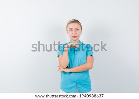  blonde woman standing in thinking pose in blue blouse and looking sensible. front view. 