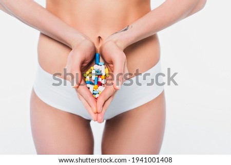 Cropped view of woman in panties holding pills isolated on white